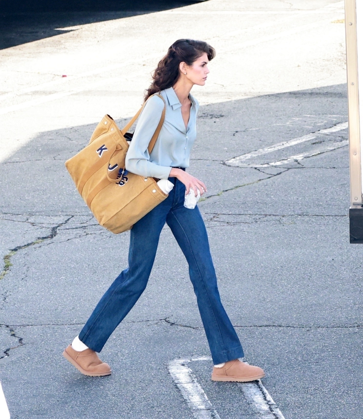 First look at Kaia Gerber in Ryan Murphy's new 80s thriller, "The Shards." Kaia showed off an uncanny resemblance to her mom, Cindy Crawford, with a classic 80s hairstyle and wardrobe. She's wearing a silk blue blouse, bootcut jeans, and Ugg Classic Micro mules.