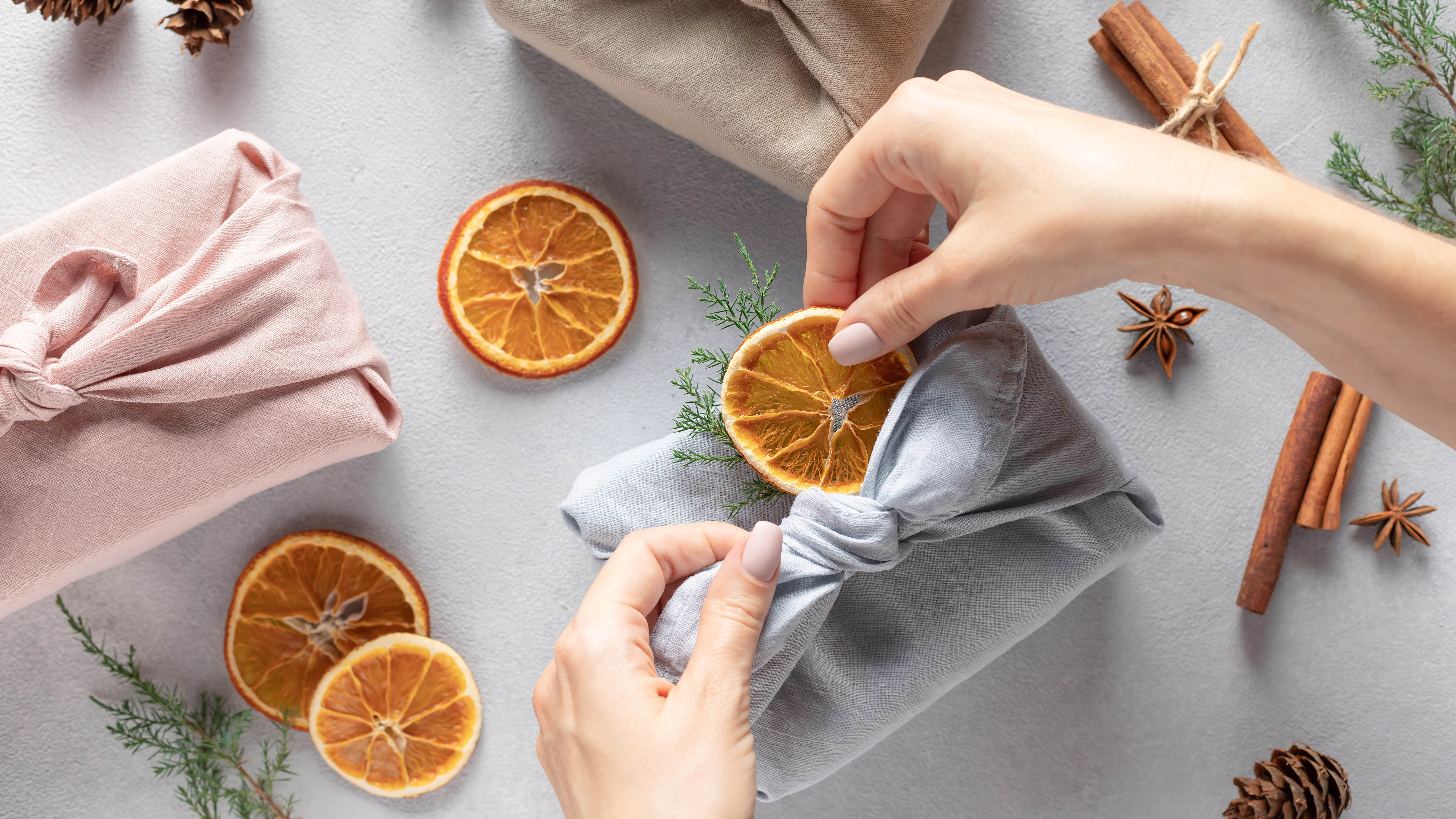 Женщина добавляет сушеный ломтик апельсина к подарку, завернутому в ткань