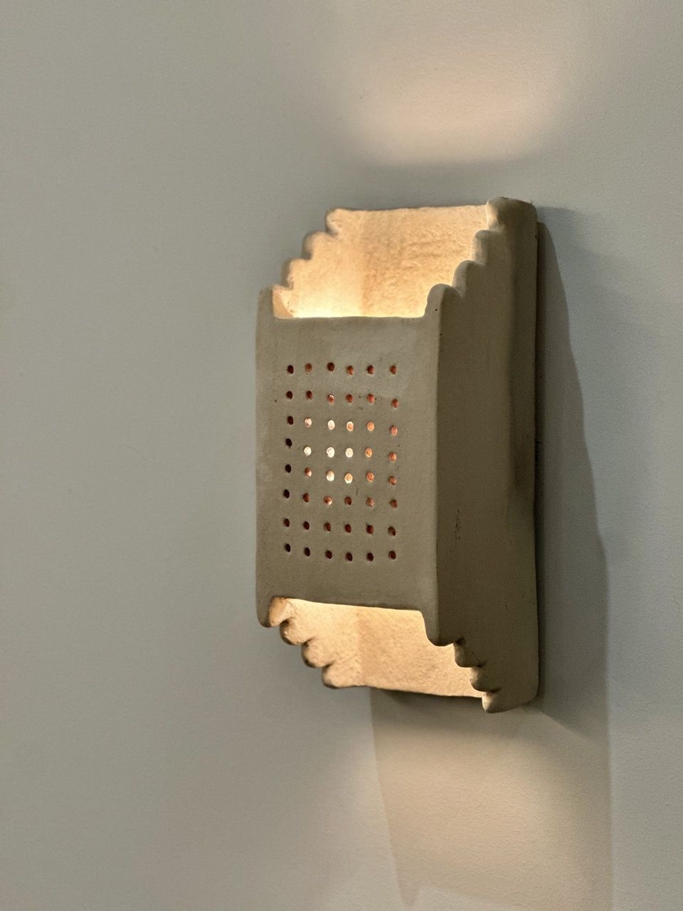 Clay light fixture from Roll and Hill, open structure with light pouring through either end, and a pattern of small holes in the front.