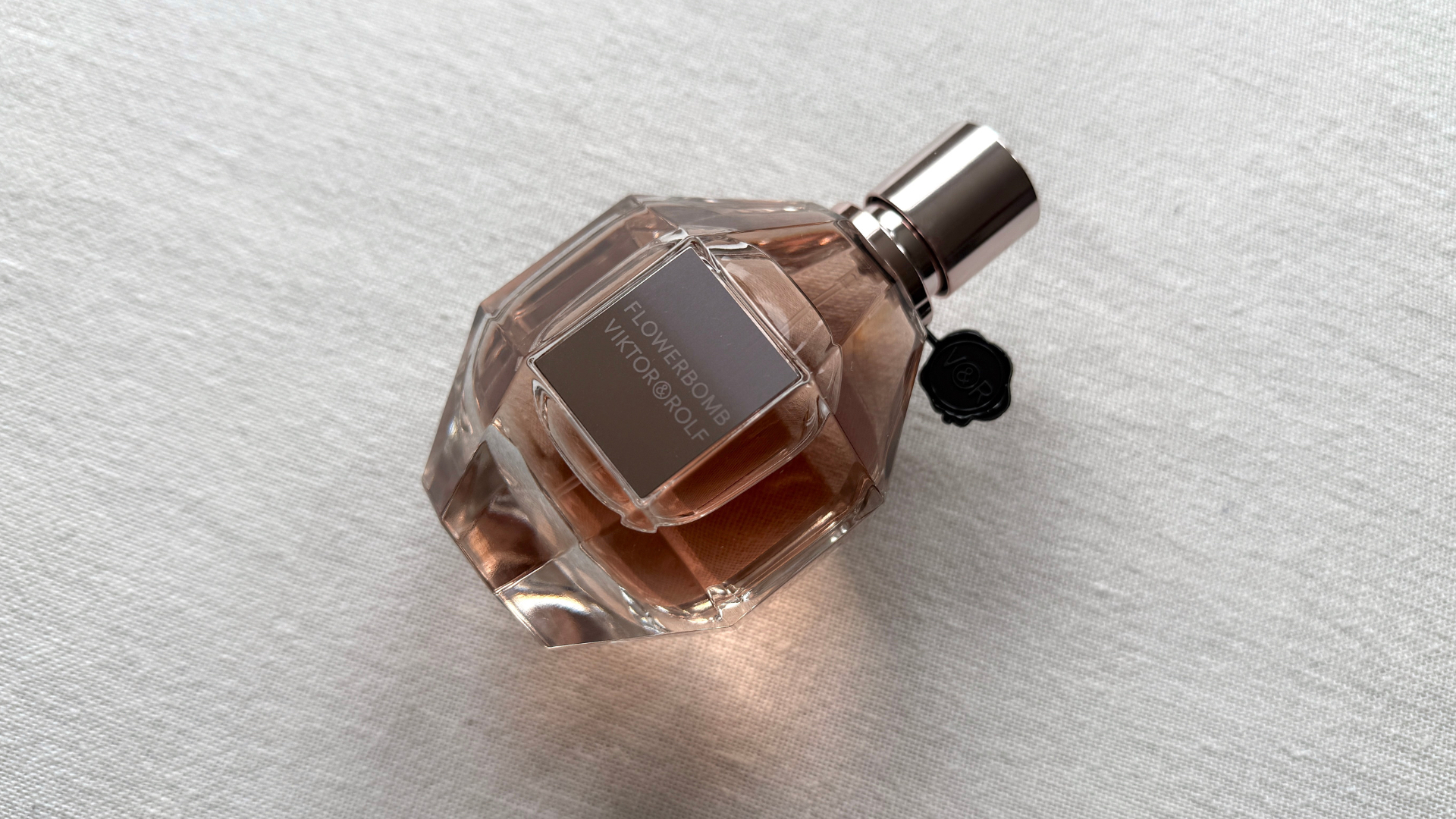 A bottle of Viktor & Rolf Flowerbomb laying at a 45 degree angle against an off-white linen background