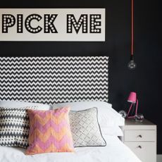 A bedroom with a black feature wall, a zigzg-print black and white headboard and a slogan print hung on the wall above the bed