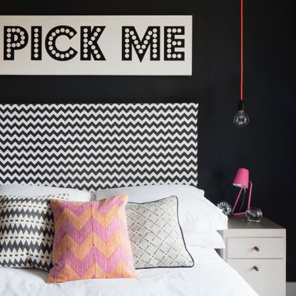 A bedroom with a black feature wall, a zigzg-print black and white headboard and a slogan print hung on the wall above the bed