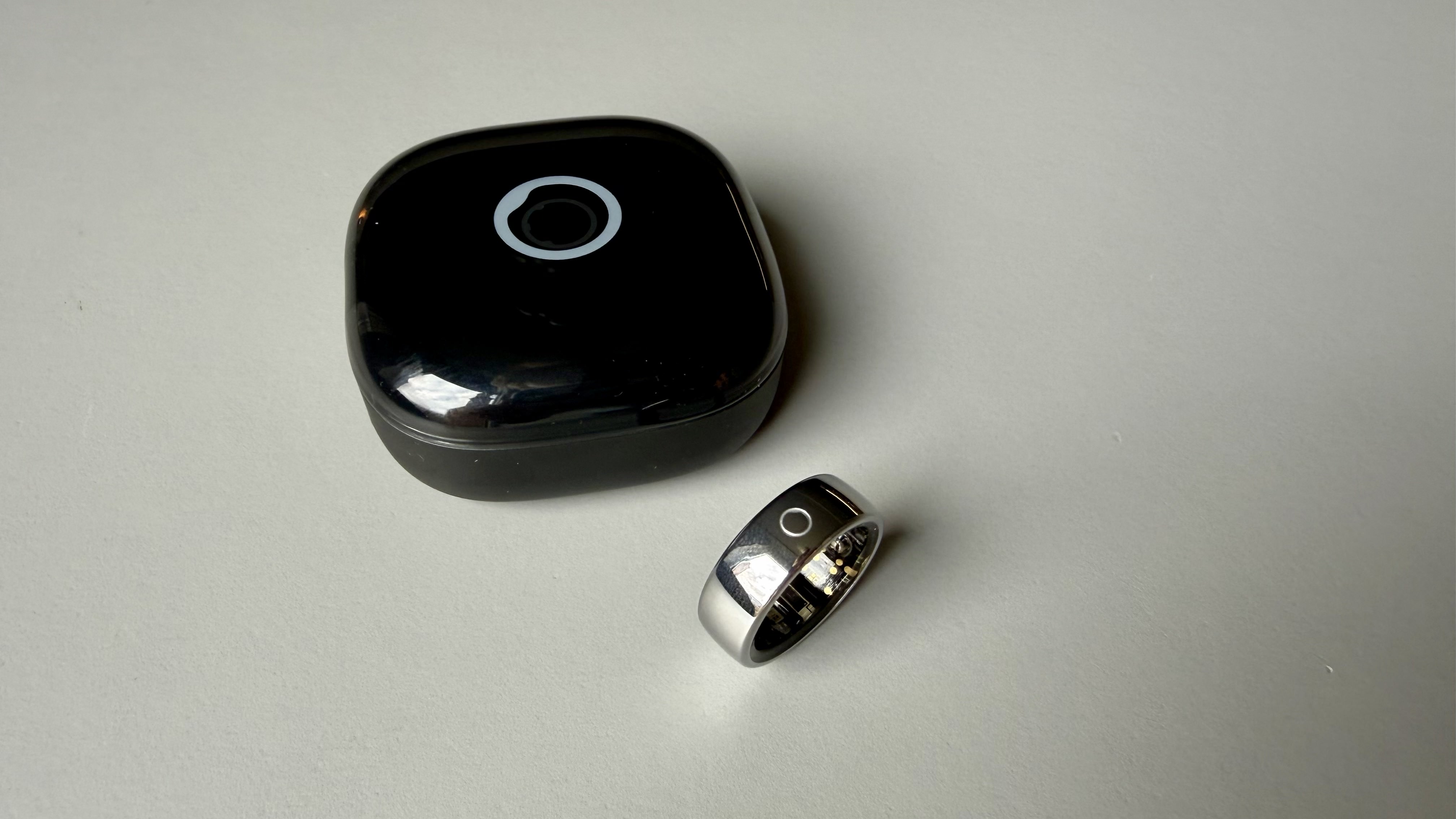 The circular ring 2 smart ring pictured on a grey surface next to its charging case
