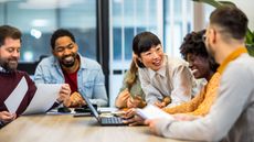 A group of smiling employees sit around a conference table for a meeting.