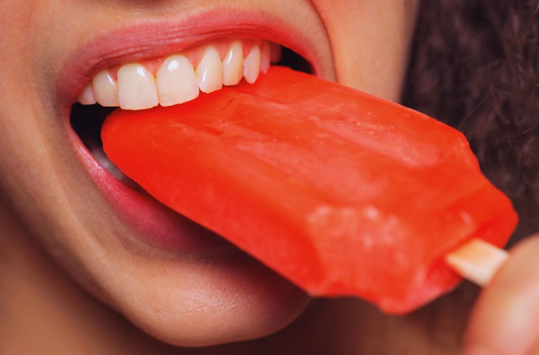 Tooth sensitivity: Close up of a woman&#039;s mouth biting into a popsicle. 