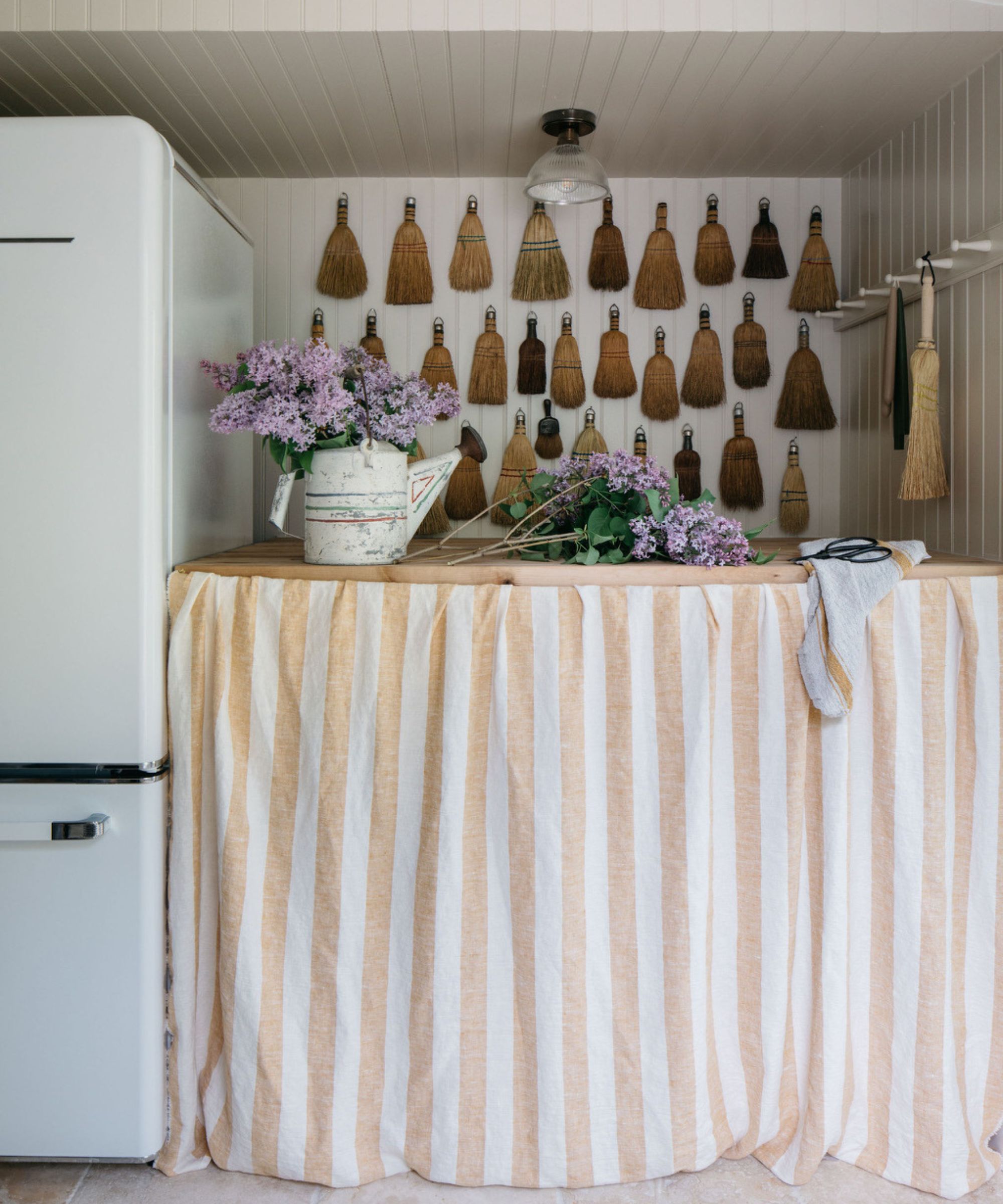 A cottage kitchen pantry with a large fridge, wooden countertops, a white and beige cabinet skirt, and walls decorated in vintage brushes