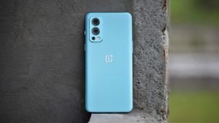 A OnePlus Nord 2 from the back, resting against a wall