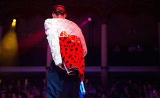 male model on a fashion week runway with his back to the camera wearing a red and black polka dot jacket