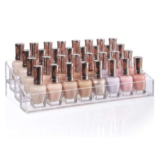 A clear 4-tier acrylic nail polish organizer with pink and nude shades of polish 