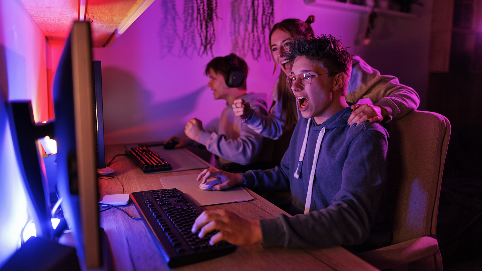 Teenage boys playing video game on desktop PC. Teenage girl is cheering for them.Canon R5