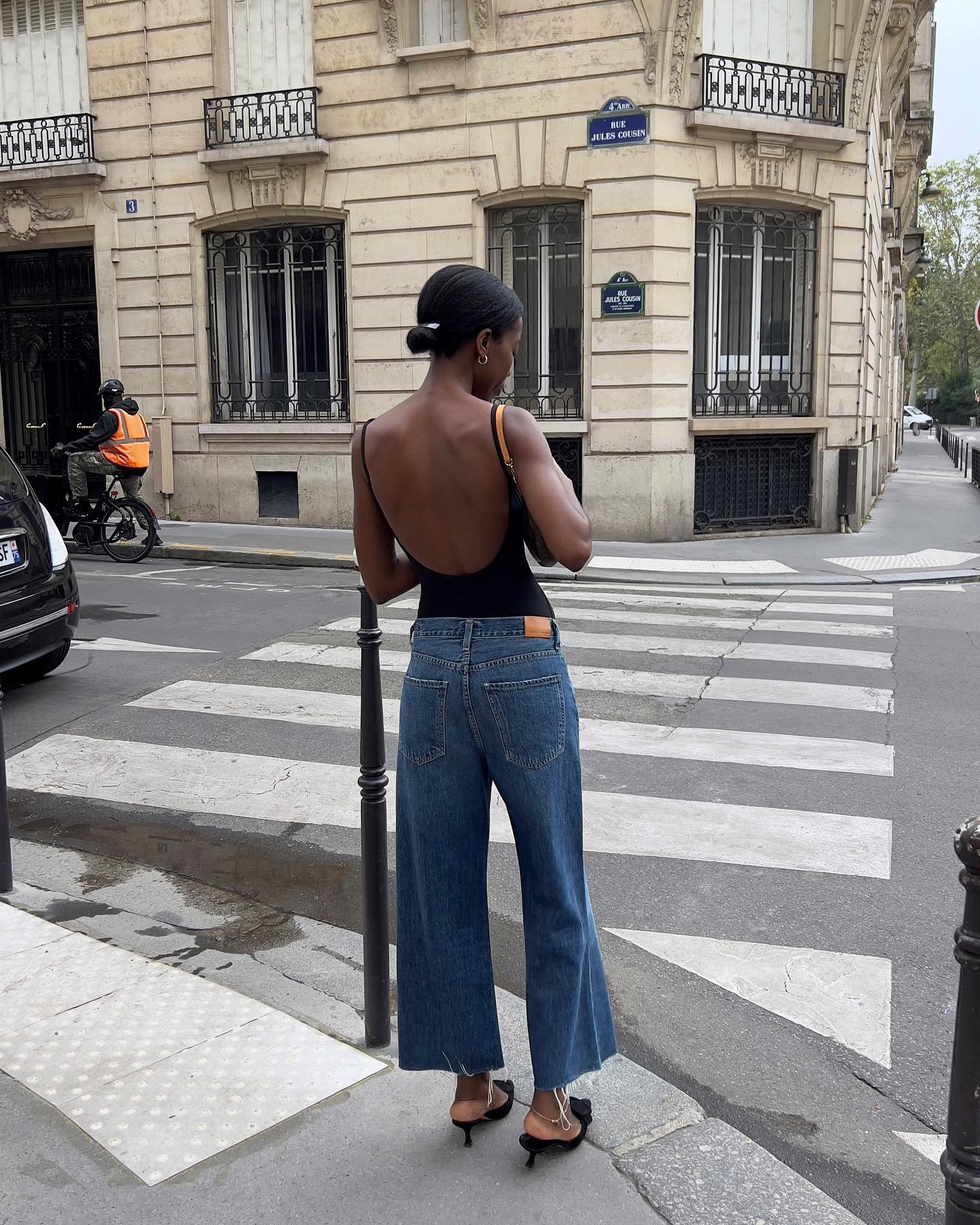 A woman wearing jeans and backless black top with black pointed-toe kitten heels.