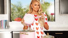 Paris Hilton in a white dress with red hearts holding sone pans from her homeware collection
