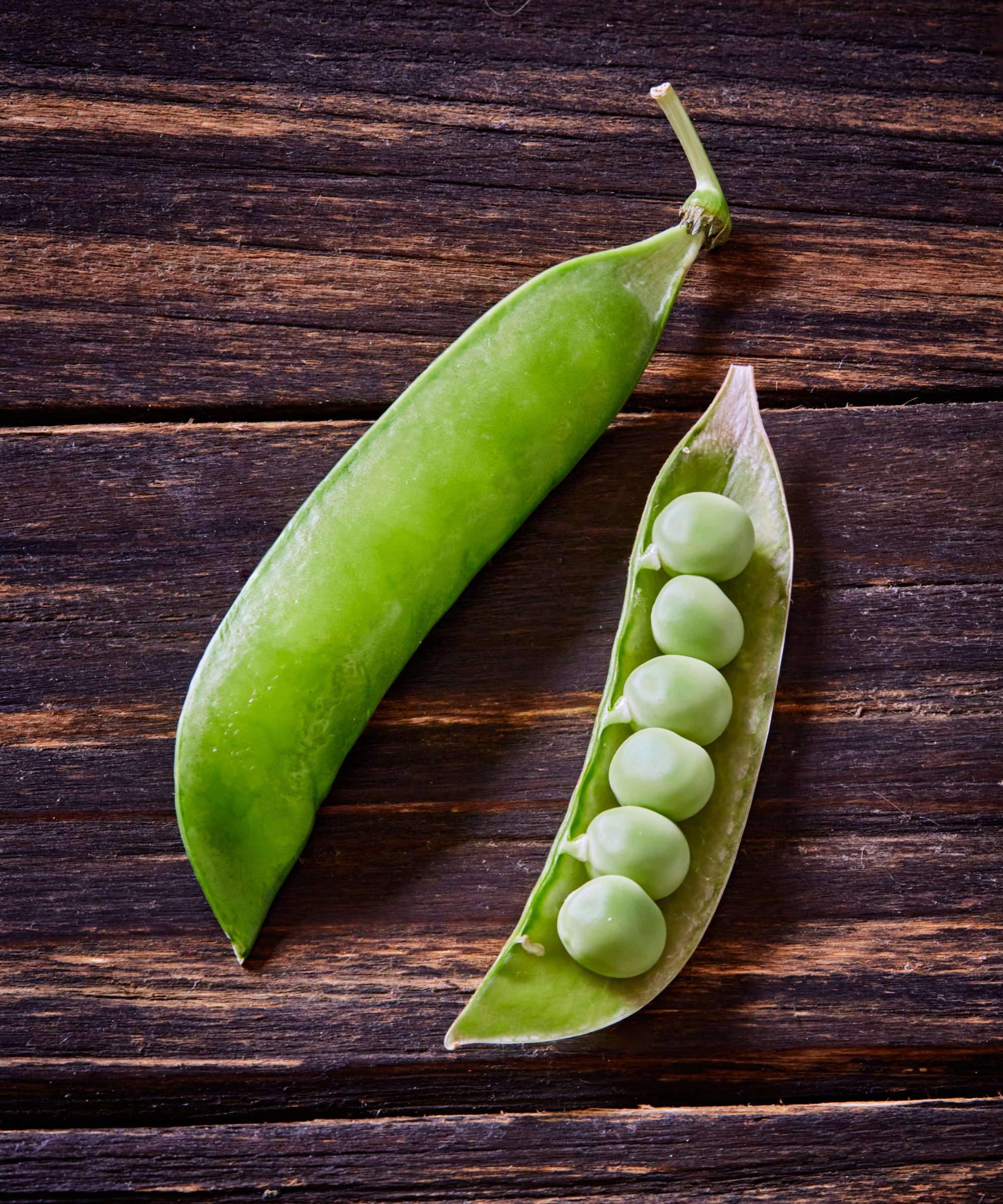 Fresh green peas in an open pod against a wooden background