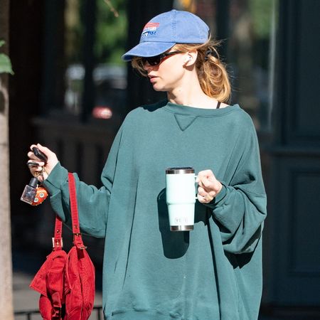 Jennifer Lawrence wearing a green sweatshirt, capri leggings, Adidas slides and a blue baseball cap in NYC