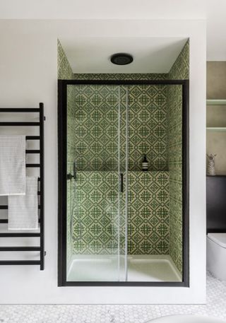 green tiled walk in shower with glass shower doors, black walls hung radiator, white tiled floor