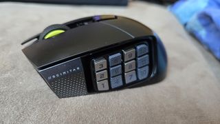 A Corsair Scimitar Elite Wireless SE gaming mouse on a carpet next to a gaming laptop and Stream Deck.