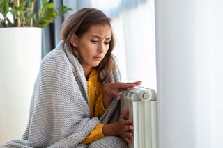 A woman next to a radiator with a blanket on looking sad