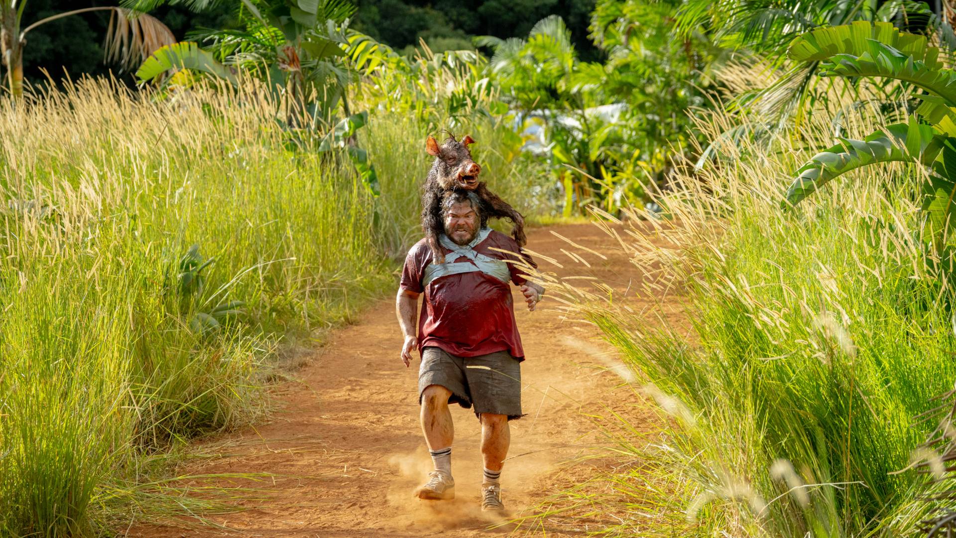 Jack Black as Doug in Anaconda (2025), running with a boar taped to his back