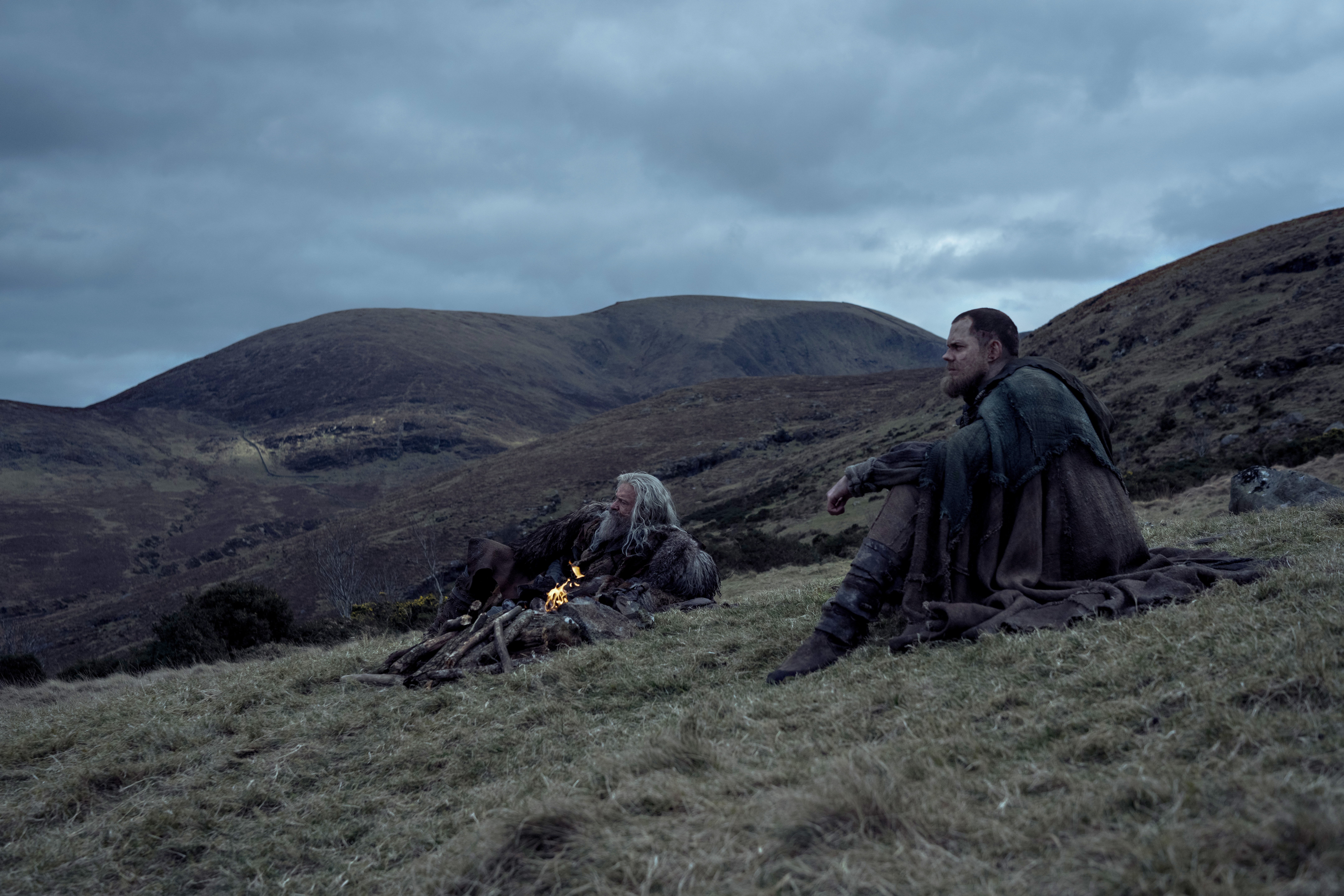 two men including hugh jackman sit on a hillside in medieval era clothing in a still from the death of robin hood