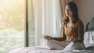 Meditating woman sat upright on bed bathed in light