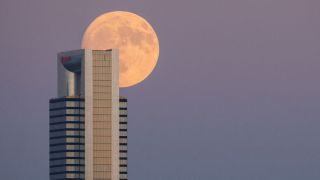 The almost full moon of August known as the Sturgeon moon rising over one of the skyscrapers of the skyline of Madrid known as the Four Towers Business Area. 