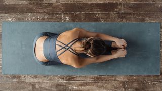 Person performing a fold over extended legs sitting on a mat during yoga on a yoga mat