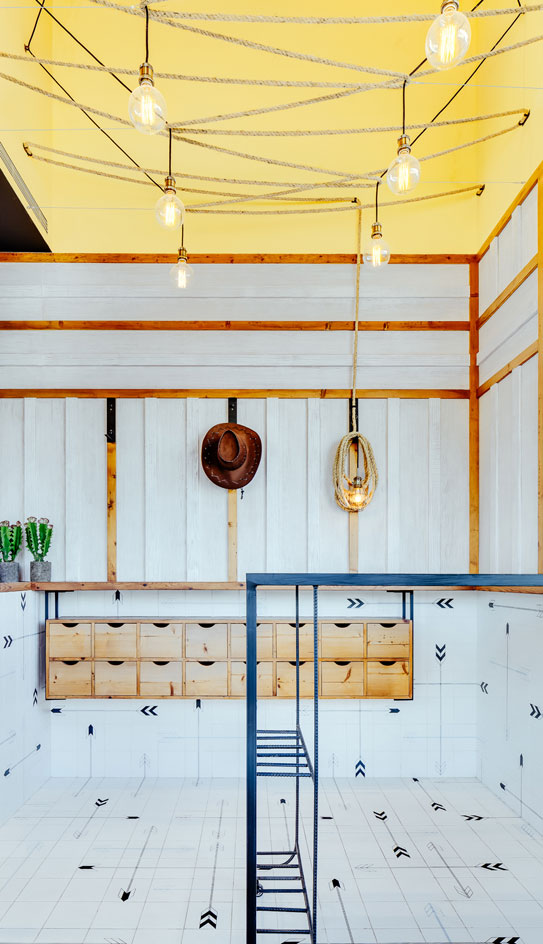 Two rows of large Edison globe lights are suspended from a woven rope that hangs lightheartedly from the mustard yellow ceiling like a lasso