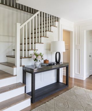 An entrance hall with black console table and white painted staircase