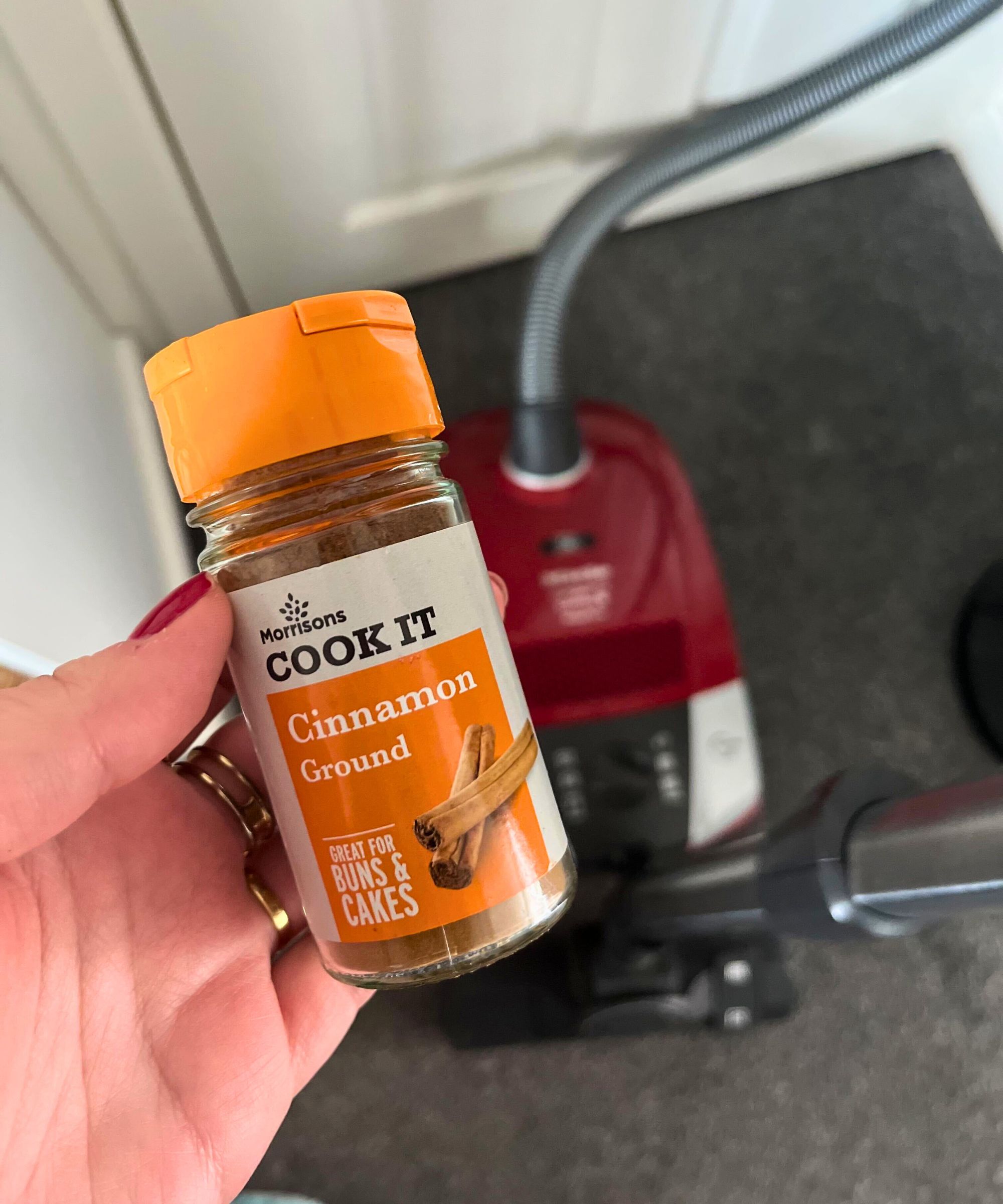 Jar of ground cinnamon held above Miele canister vacuum on gray carpet