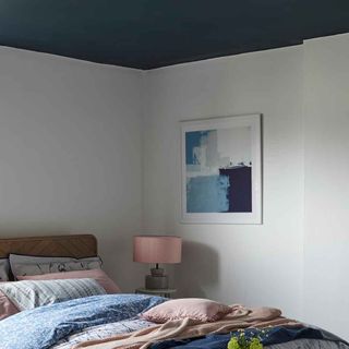 bedroom with blue ceiling and white wall with painting on wall and pillows on bed