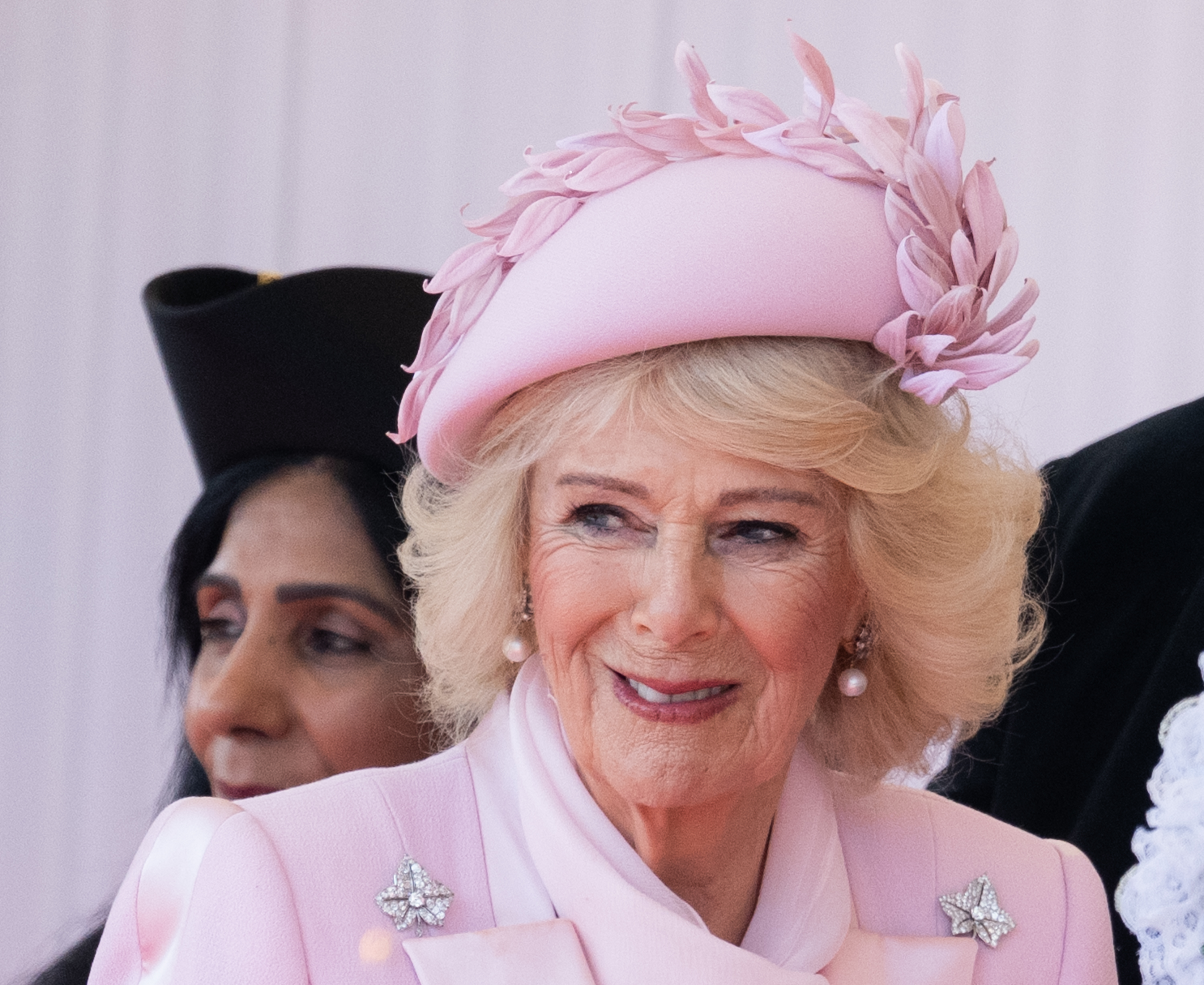 Queen Camilla wearing a pink coat and hat and smiling