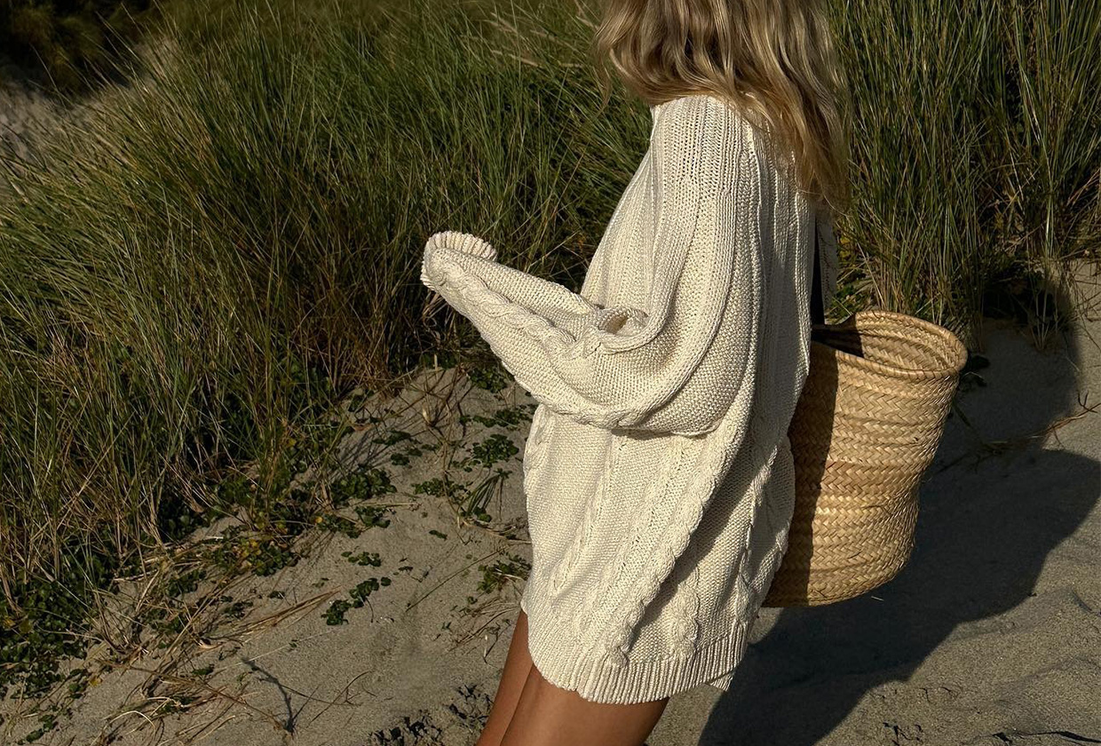 Lucy Williams wearing a loose cotton sweater with a straw bag on the beach.