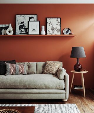 A beige sofa in front of a red wall with a single black shelf displaying artwork