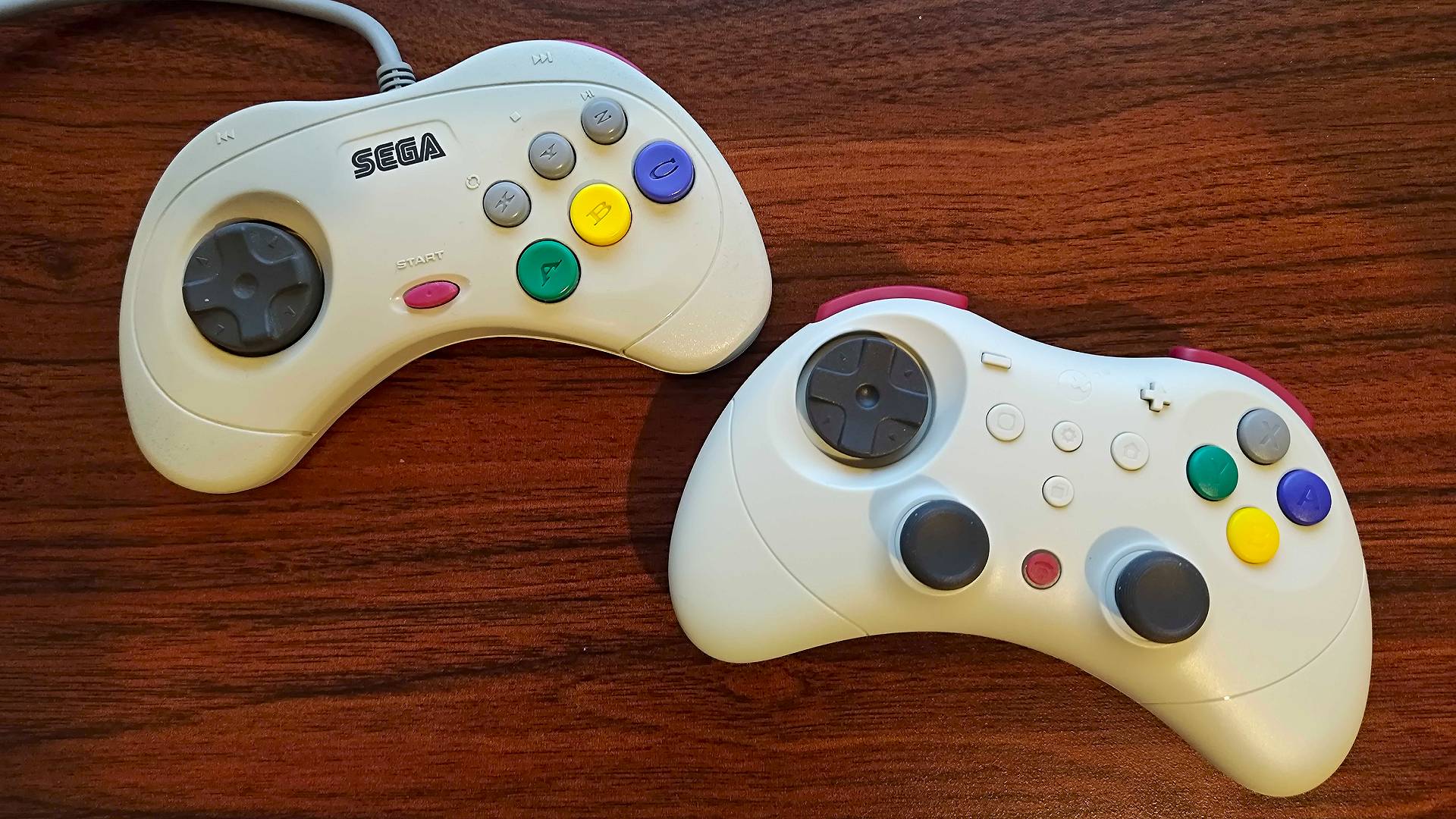 Sega Saturn gamepad next to Gulikit Elves 2 Pro controller on woodgrain desk.