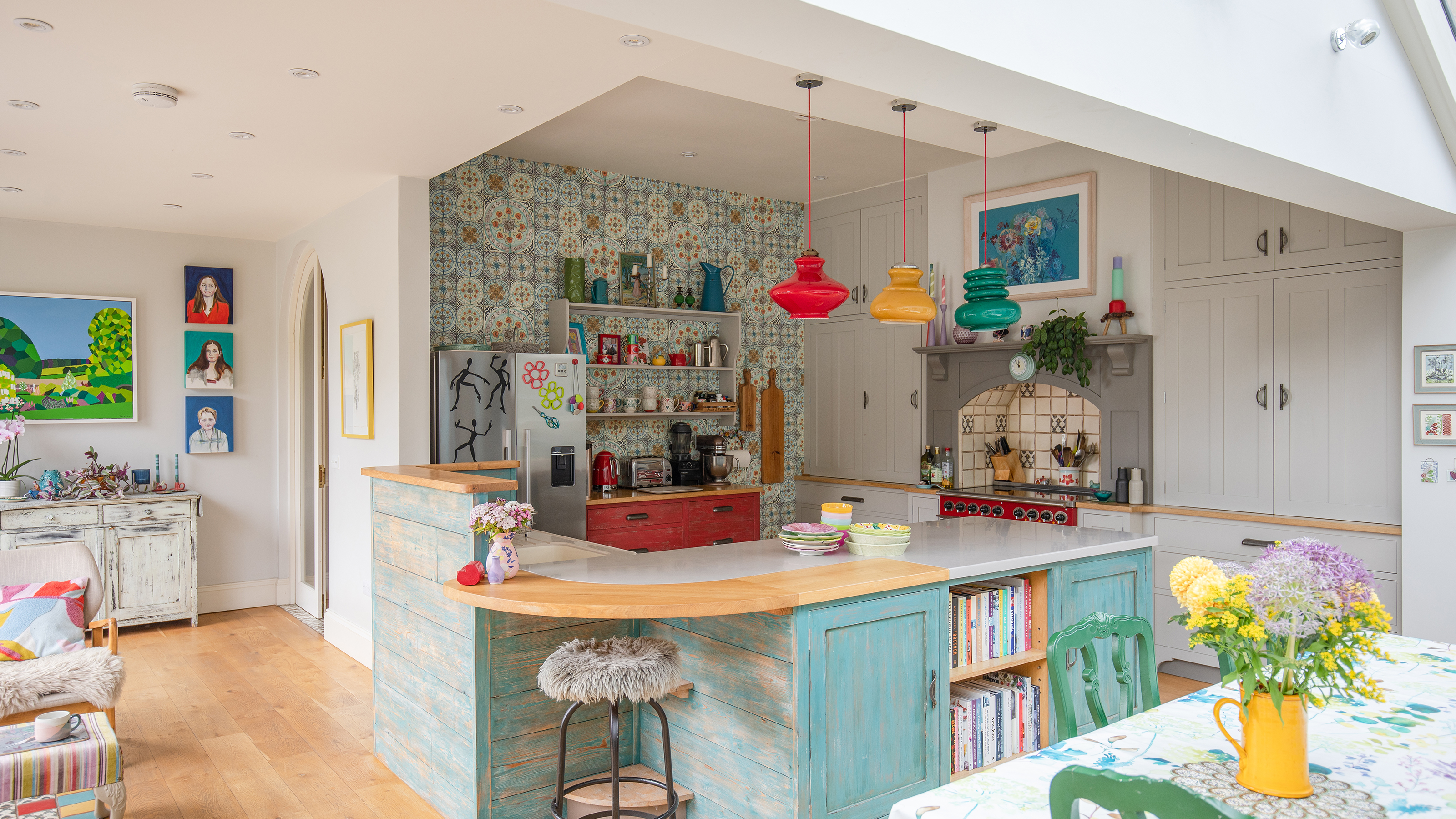 open plan kitchen diner with decorative wall tiles, colourful glass pendant lights and turquoise cupboards