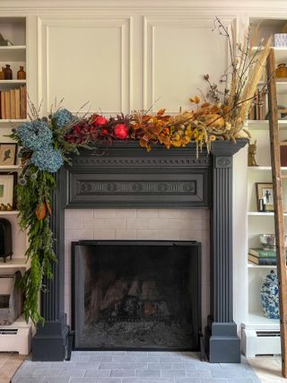 A fireplace decorated for fall with an autumnal garland draped across the mantel