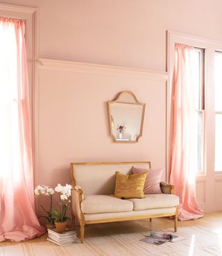 A living room painted pink with a small cream loveseat
