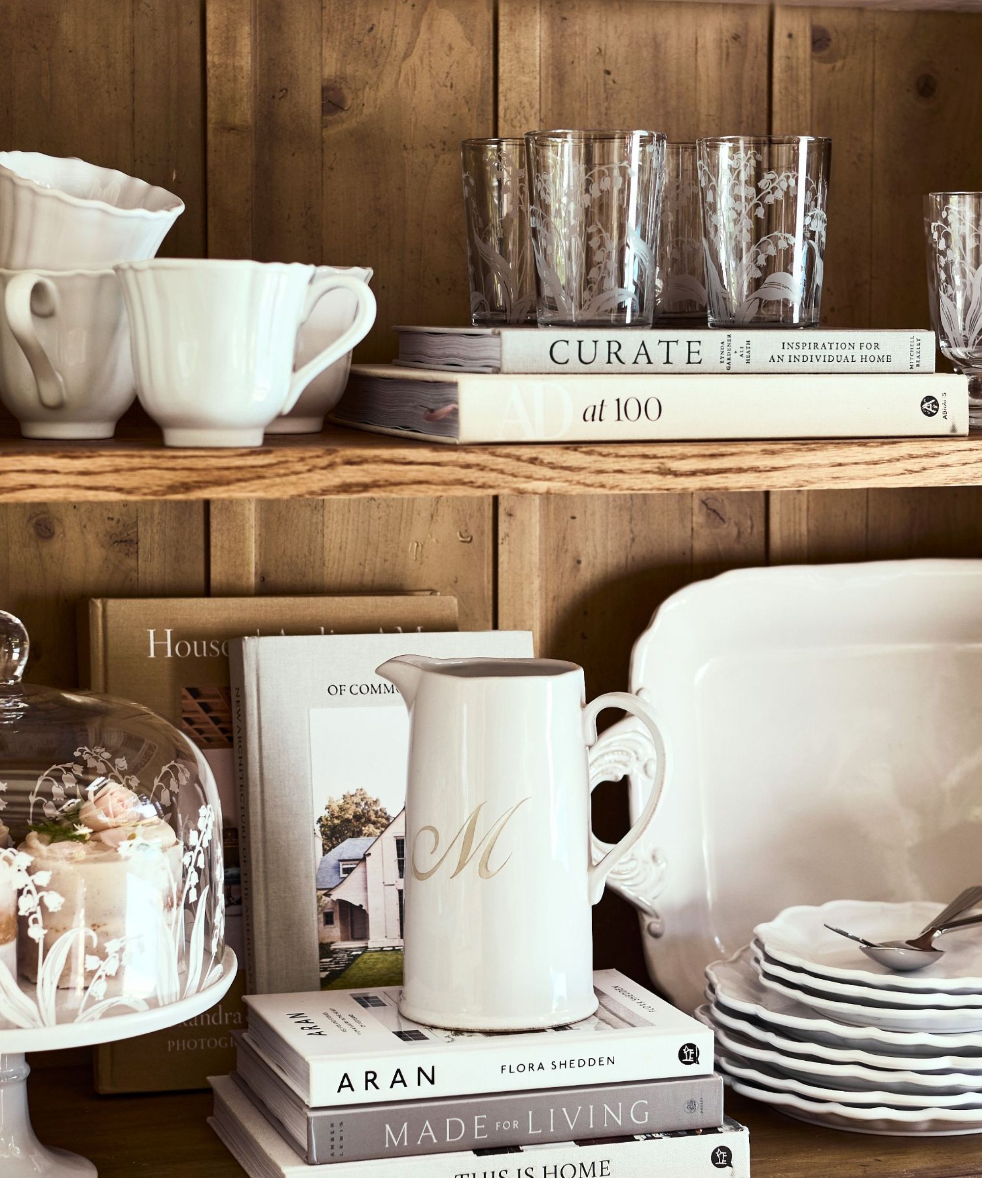 White dinnerware set on wood shelf with interior design books and floral glassware