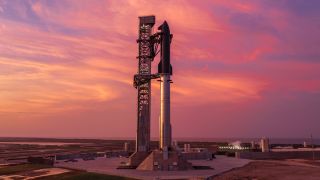 A towering SpaceX Starship rocket stands ready for Flight 13 launch amid a stunning pink sky in twilight.