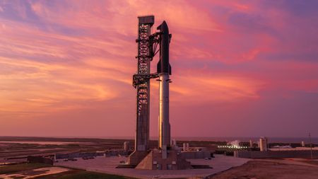 A towering SpaceX Starship rocket stands ready for Flight 13 launch amid a stunning pink sky in twilight.