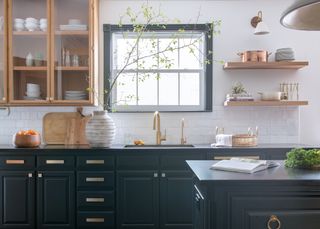 kitchen with dark cabinets, dark countertop, white metro tile backsplash, white walls, dark window frame, open shelving, wood and glass wall cabinet, kitchen island, copper and wood accessories