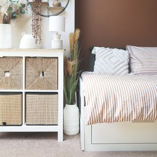 White and terracotta painted bedroom with a pull-out bed and a storage unit with wicker storage baskets in it