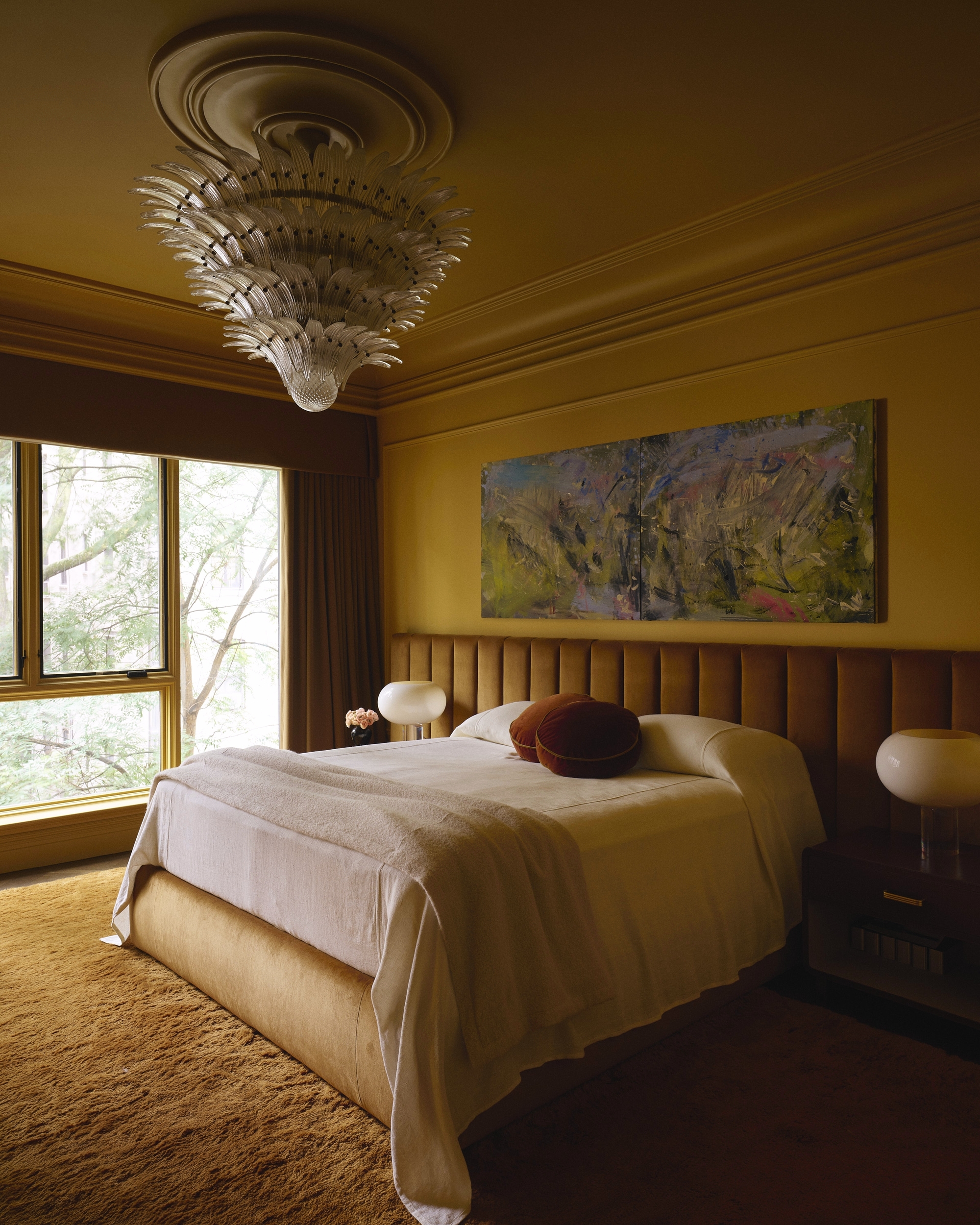yellow color drenched bedroom with vintage chandelier, extended headboard, orange shag carpet and bed made with cream bedcover and terracotta cushions