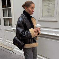 Woman wearing a black shearling coat, jeans, and a Chanel bag