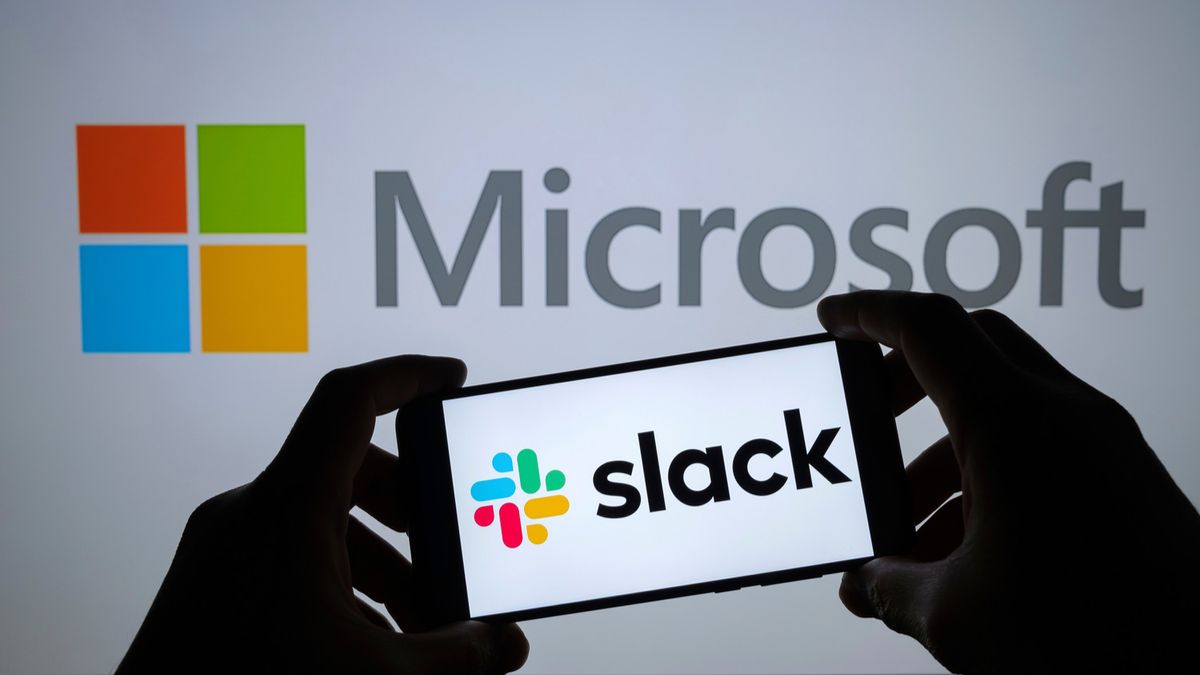 A person holding a smartphone with a Slack logo against a larger Microsoft logo