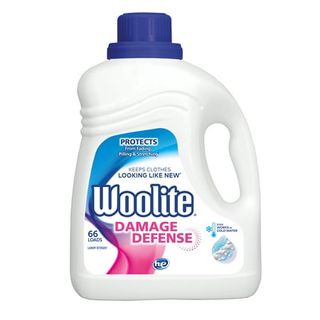 A large white plastic detergent bottle with a handle and a dark blue lid. White label with Woolite branding with a streak of pink and blue running up the side of the label. 