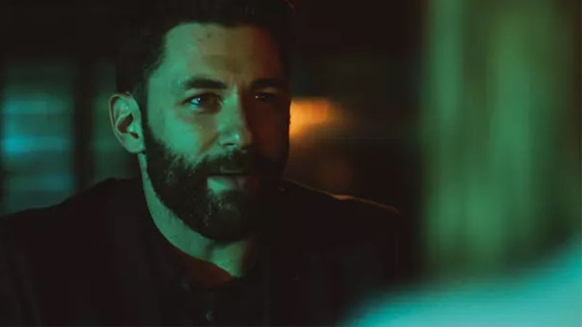 A man with a beard and black collared shirt smiles 