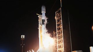 a rocket blasts off a launch pad into a black sky.
