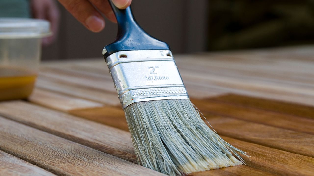 person using a paintbrush to stain wooden outdoor furniture