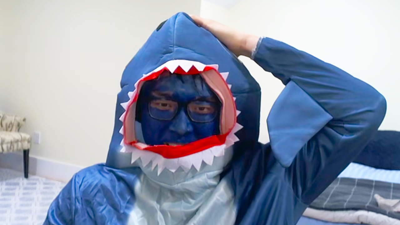 A screencap of a Path of Exile 2 stream by XTheFarmerX on YouTube. The streamer is wearing a blue shark onesie with a hole for their face in the mouth. Their face is painted blue to match, and they&#039;re holding the top of their head.